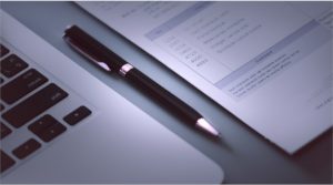Um laptop na mesa, uma caneta e um contrato na reunião com o detetive particular em São Paulo - Expert Detetives.
